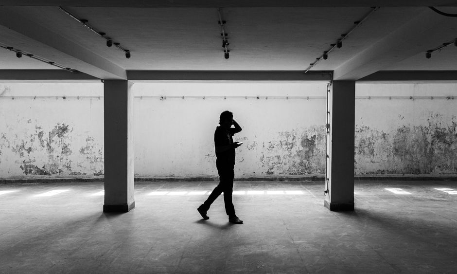 A solitary man in a suit is dwarfed by an imposing, minimalist concrete building, visually representing the feeling of being trapped within a successful but rigid career structure.
